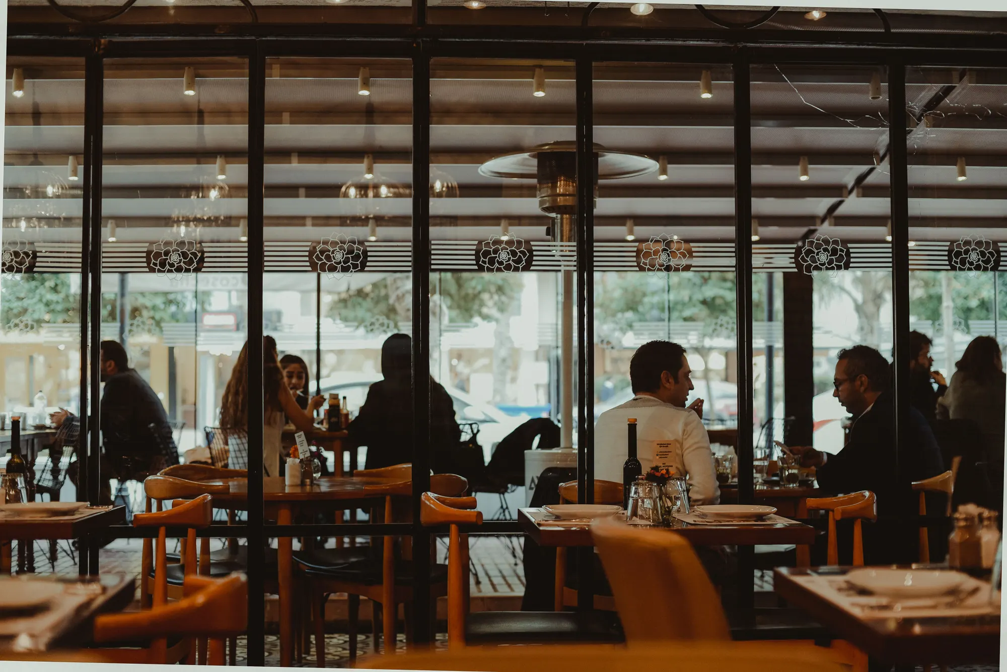 A glass-walled restaurant dining room, guests at every table as the light goes down